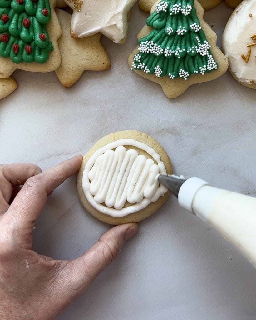 Filling in the outline of frosting on a round sugar cookie.