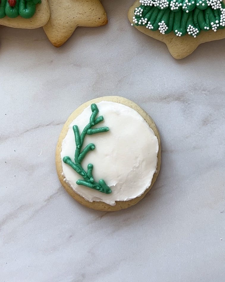 Round sugar cookie with white frosting and green frosting like Christmas holly.