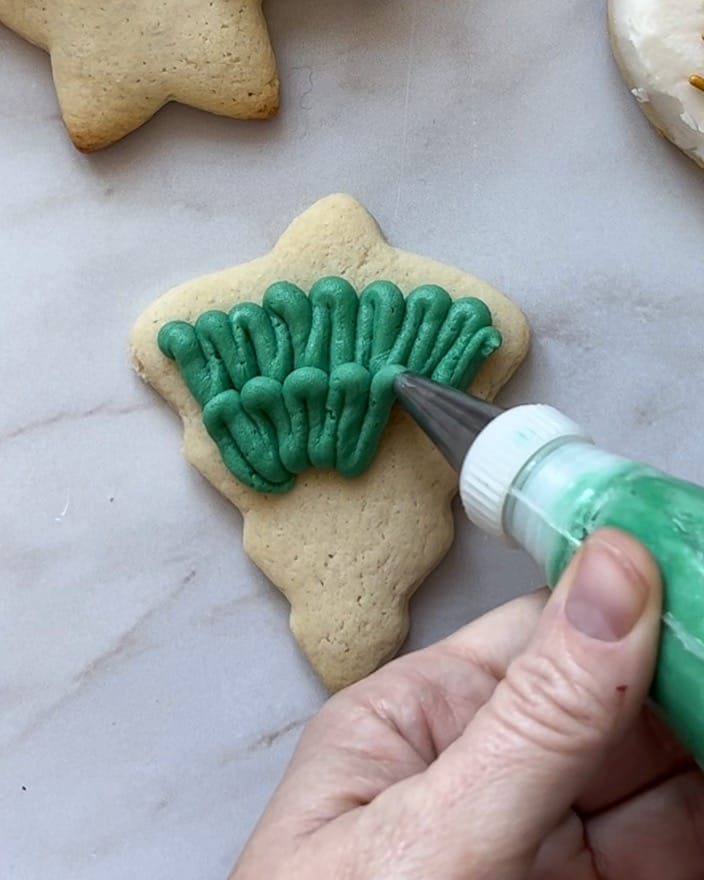 Using a piping bag and tip to frost a Christmas tree sugar cookie.