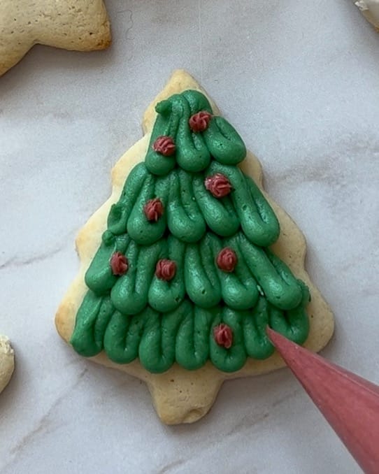 Adding buttercream decorations to a christmas tree sugar cookie