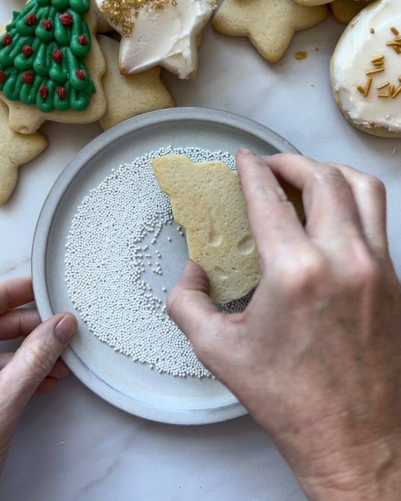 Dipping a christmas tree sugar cookie in sprinkles.