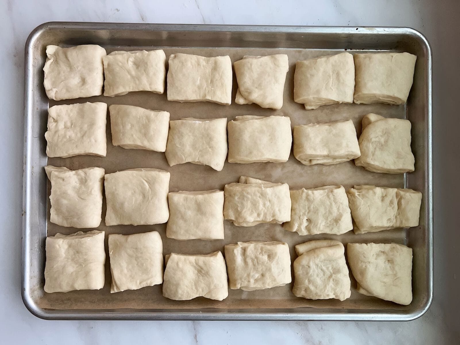 Full pan of Parker House Rolls rising in a baking sheet.