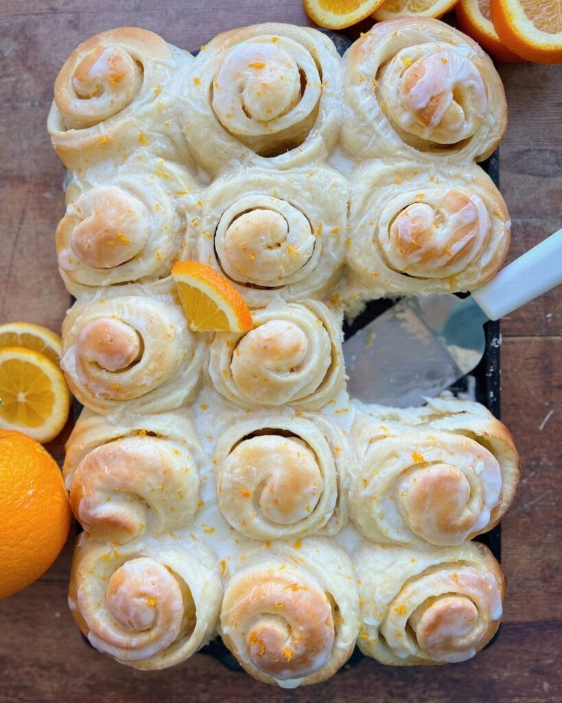 Frosted orange sweet rolls in a pan.
