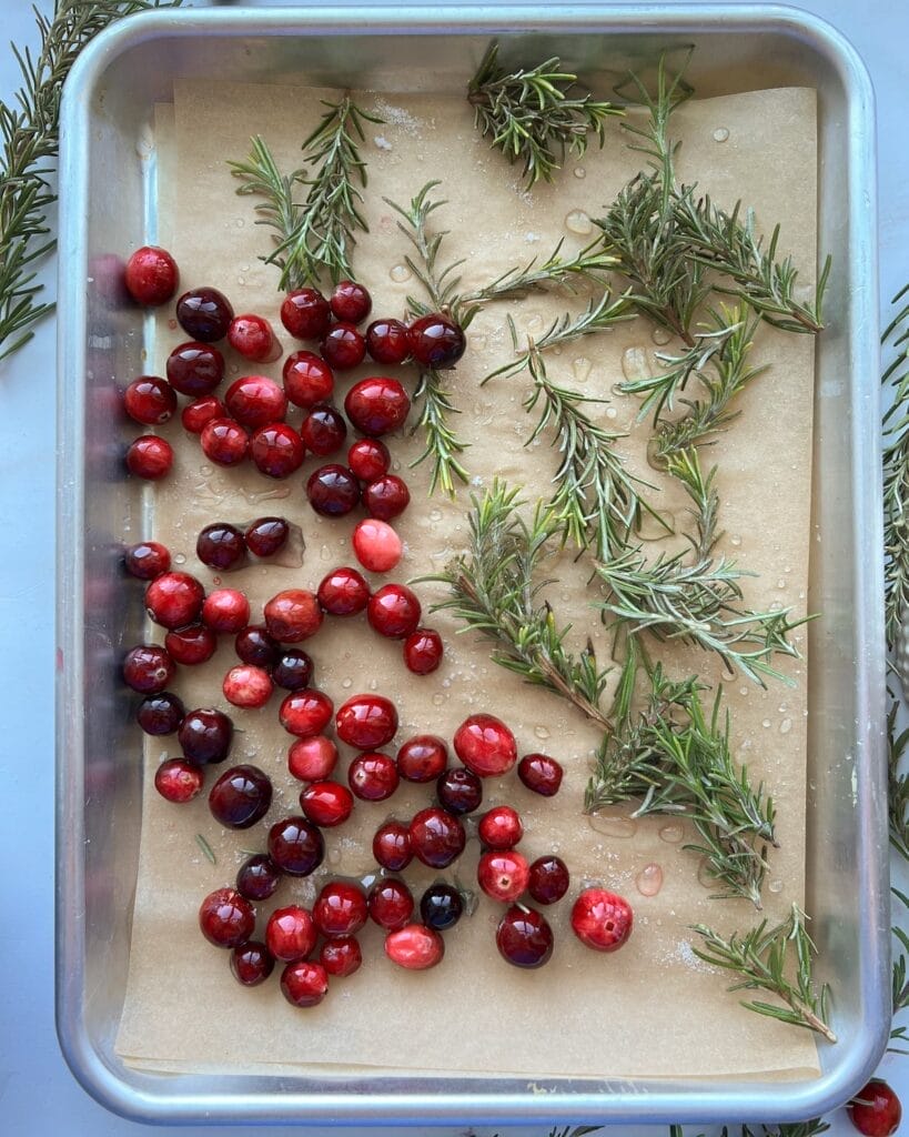 Cranberries and rosemary twigs on a parchment lined baking sheet.