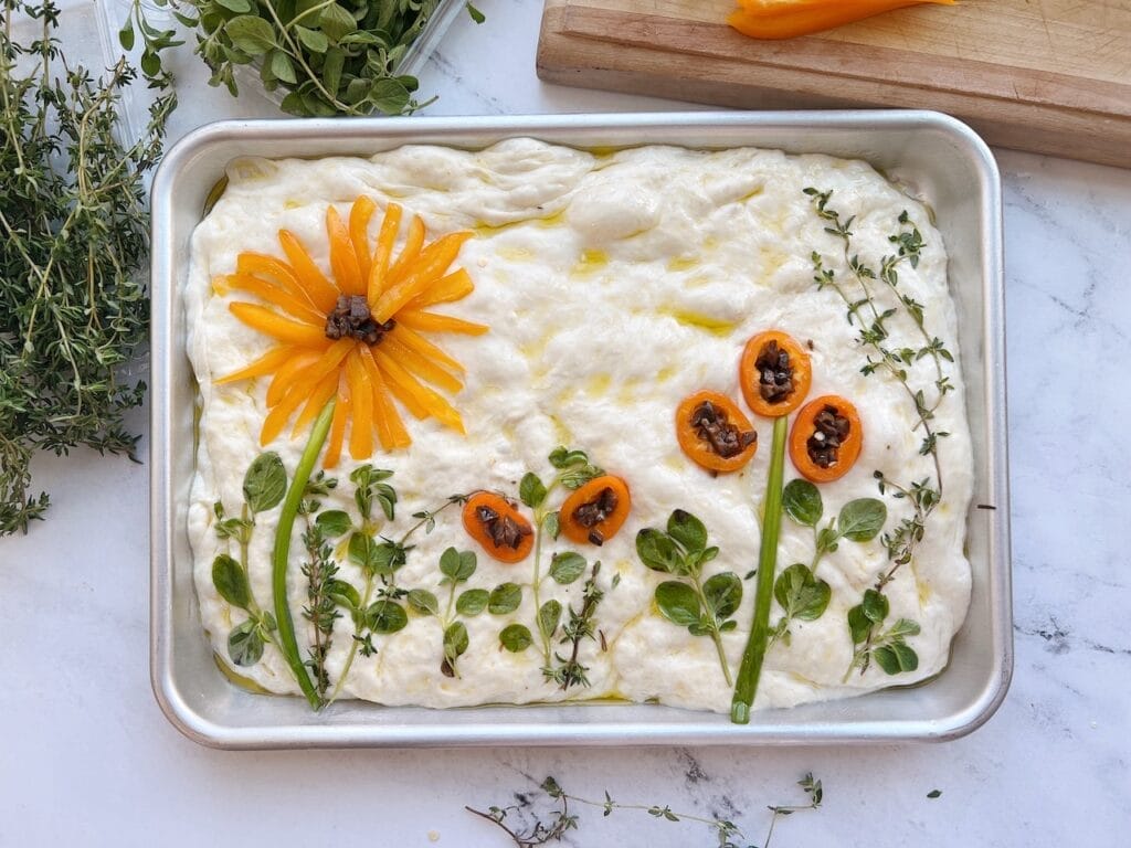 Focaccia dough in a pan with vegetables arranged like a flower garden.