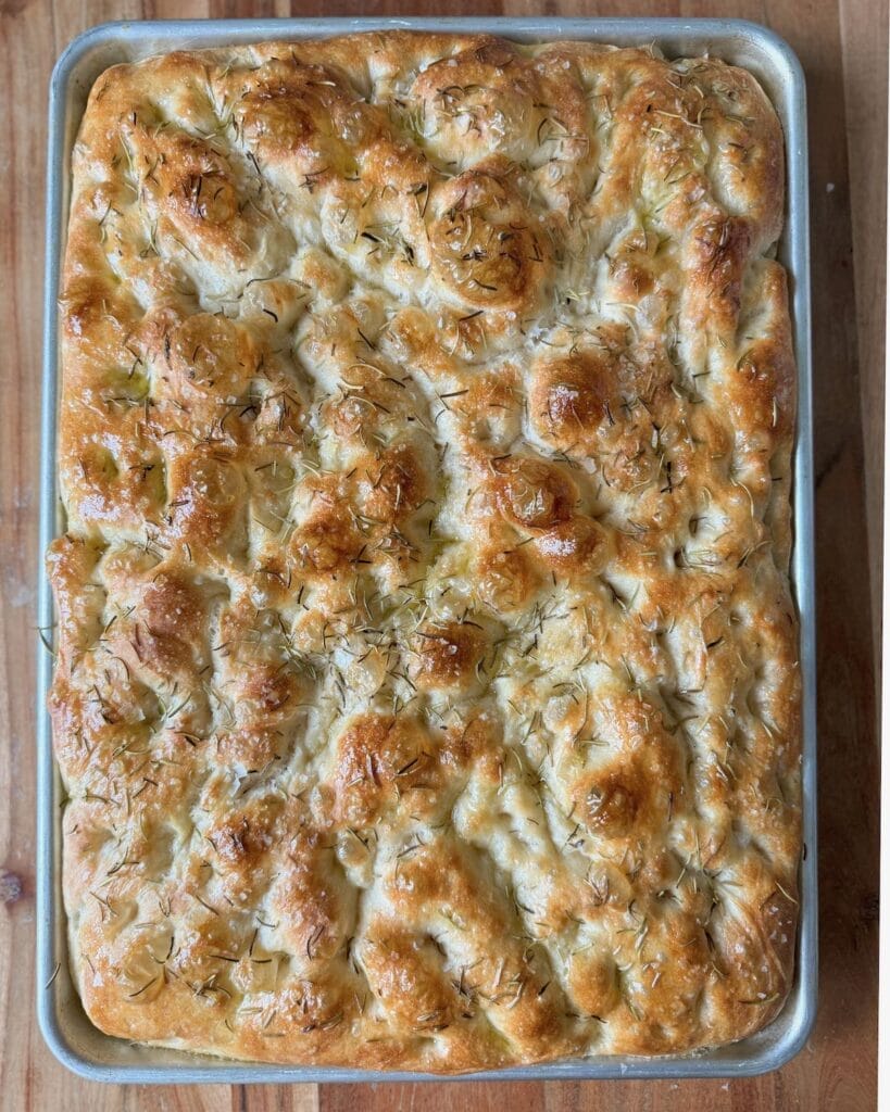 A baking sheet of baked focaccia with rosemary on top.