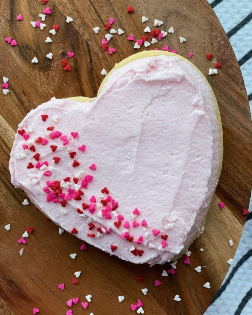Frosted sugar cookie with pink frosting and heart sprinkles.