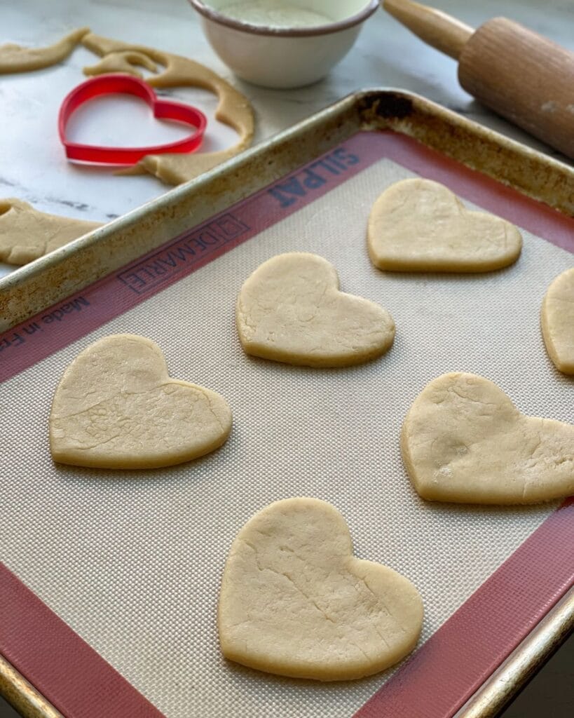 Heart shaped sugar cookies on a baking sheet lined with a silicone baking mat.