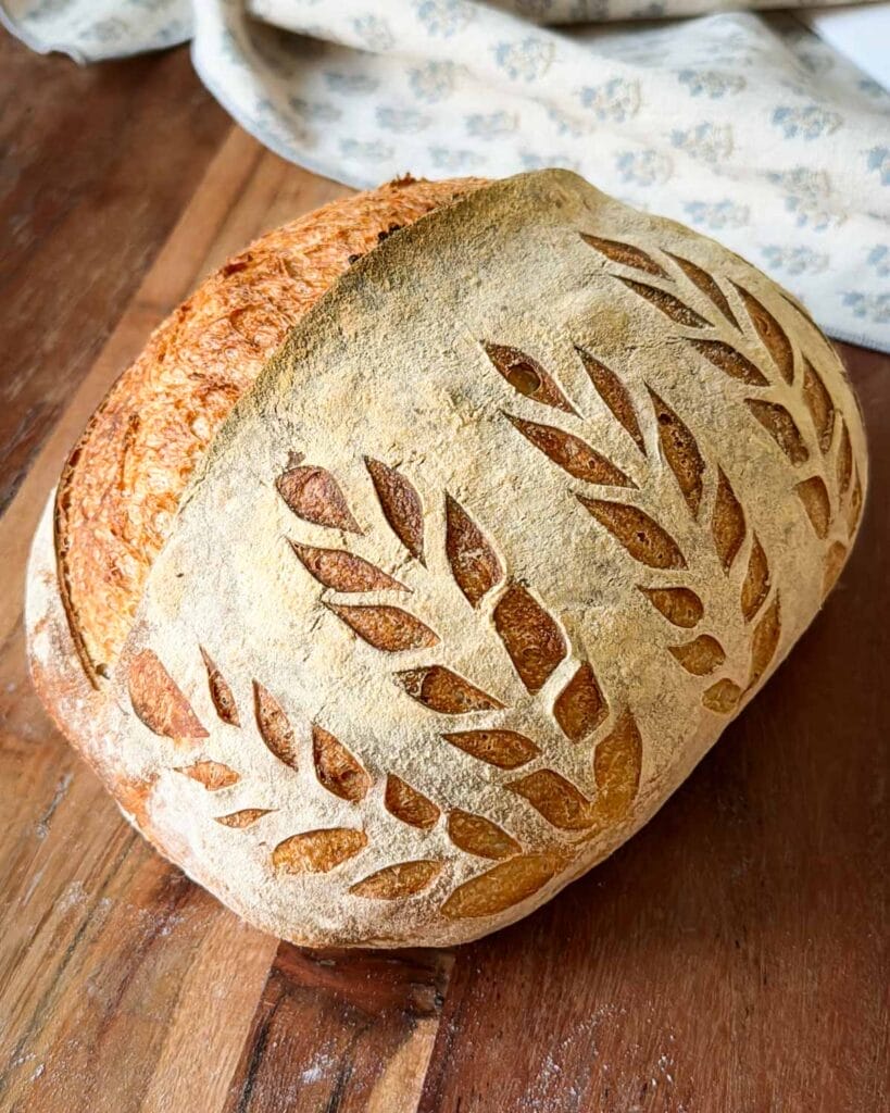 A loaf of sourdough with wheat stalks scored into the side.